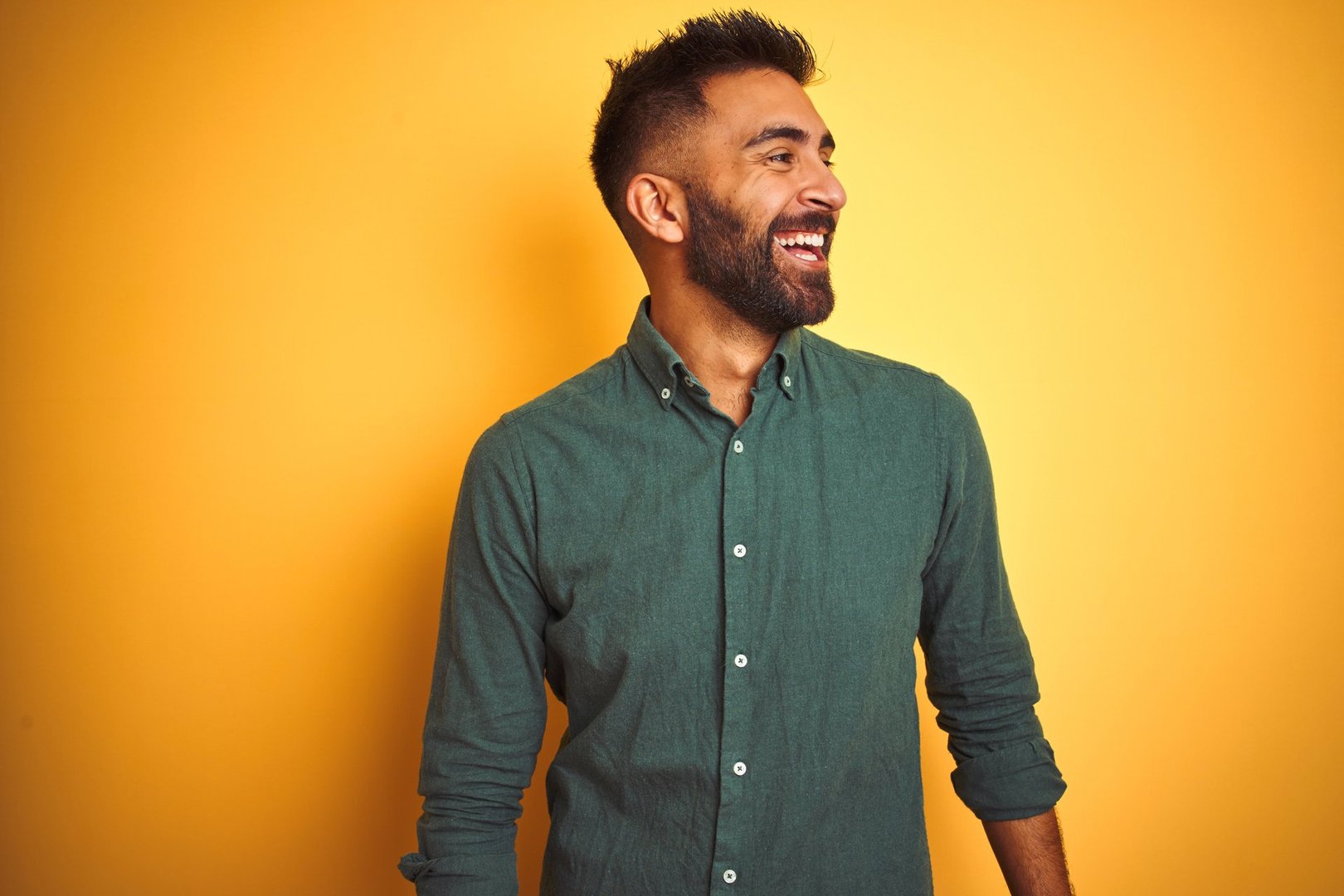 Young indian businessman wearing elegant shirt standing over isolated white background looking away to side with smile on face, natural expression. Laughing confident.