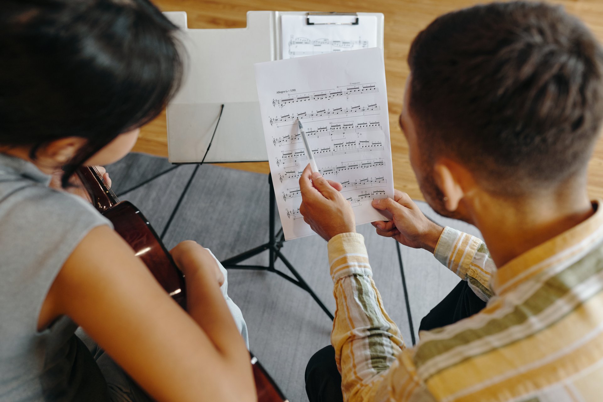 Musicians collaborating while reading sheet music in professional studio setting Musician on left holding guitar while another musician points at music notes engaging in collaboration