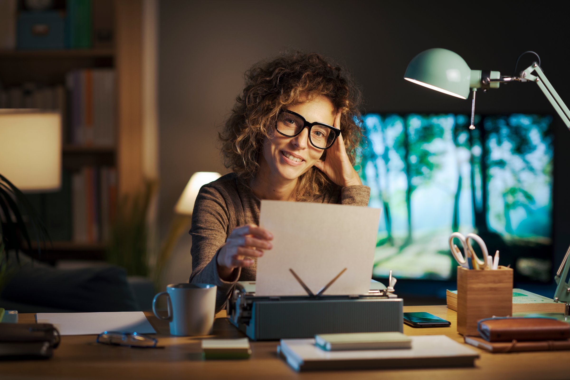 Portrait of a happy creative writer in her home office, she is using a vintage typewriter