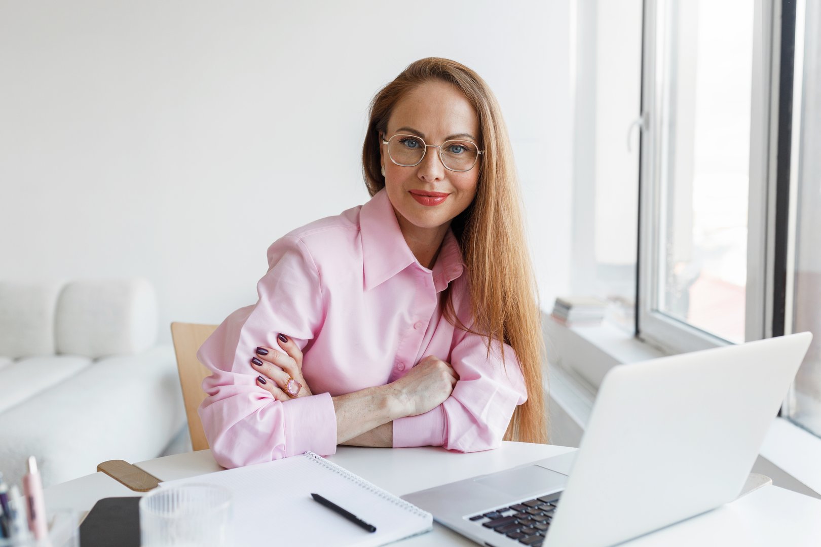 Successful and confident female therapist, psychologist sitting at table in her office or cabinet with folded arms and looking at camera, ready to give you working tips to cope with frustration
