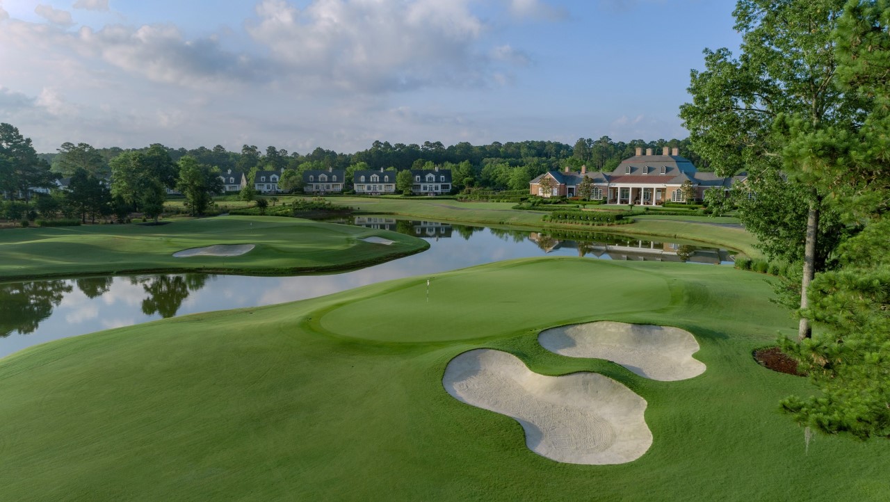 Scenic golf course with sand traps, manicured greens, and a clubhouse near a reflective pond.