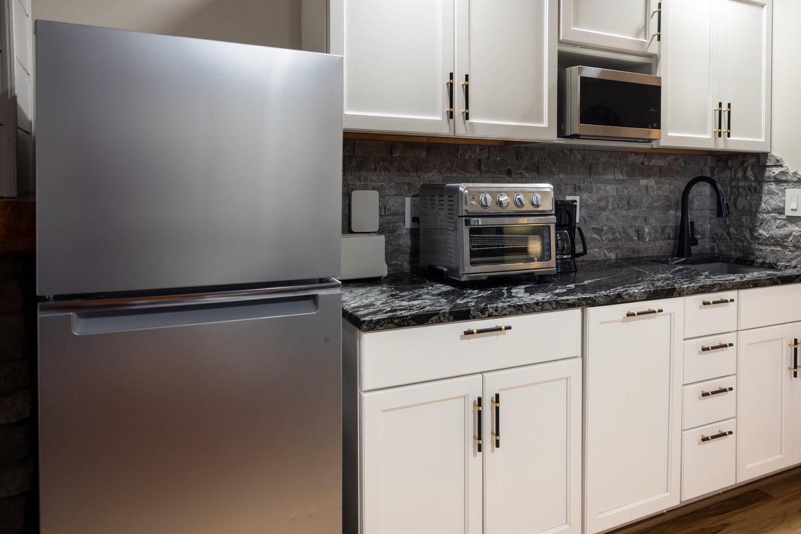 Small kitchenette with refrigerator, toaster oven, microwave, sink, and cabinets