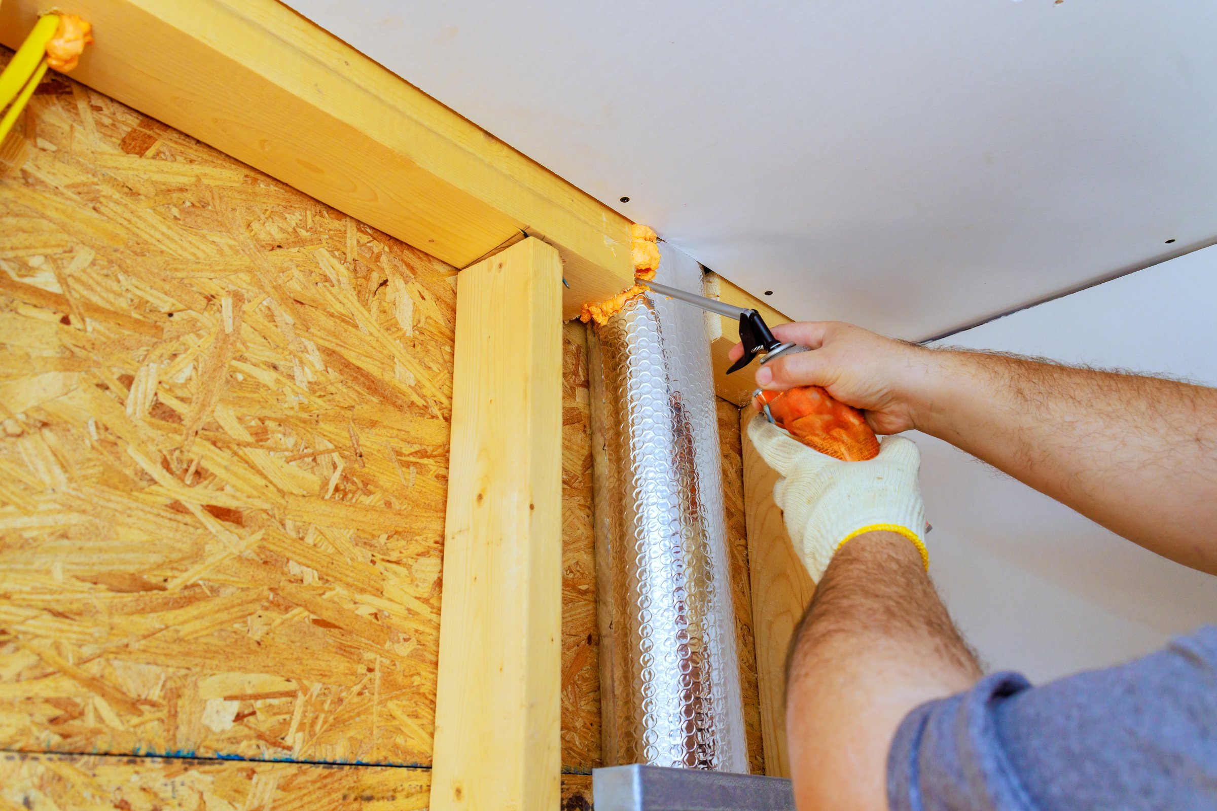 Worker is applying foam insulation to vent pipe in residential area, on energy efficiency during renovations.