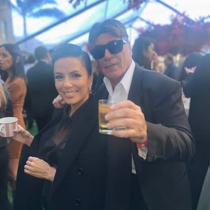Two people at an event, one holding a drink. They are dressed formally and appear to be enjoying the occasion.