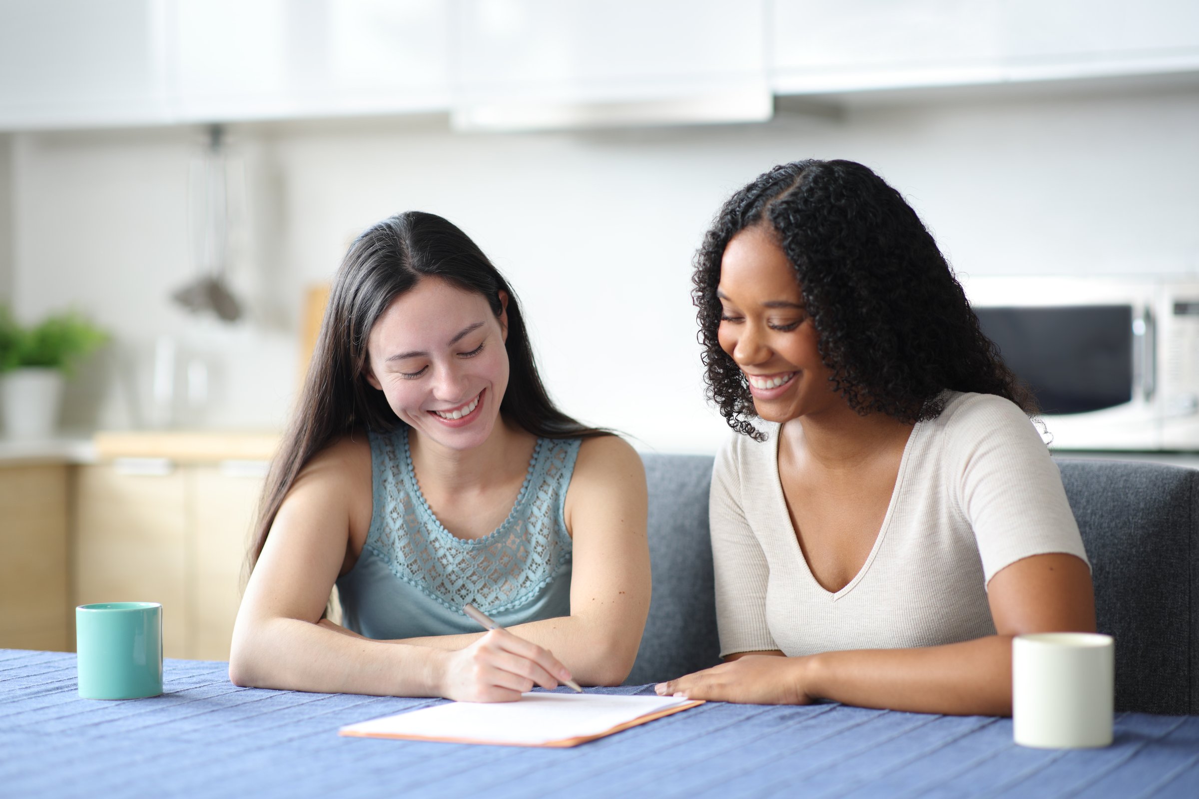 Happy interracial roommates signing paper contract at home