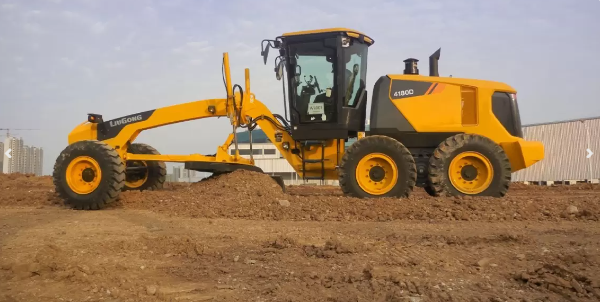 Yellow construction grader leveling dirt at a construction site with a clear sky in the background.