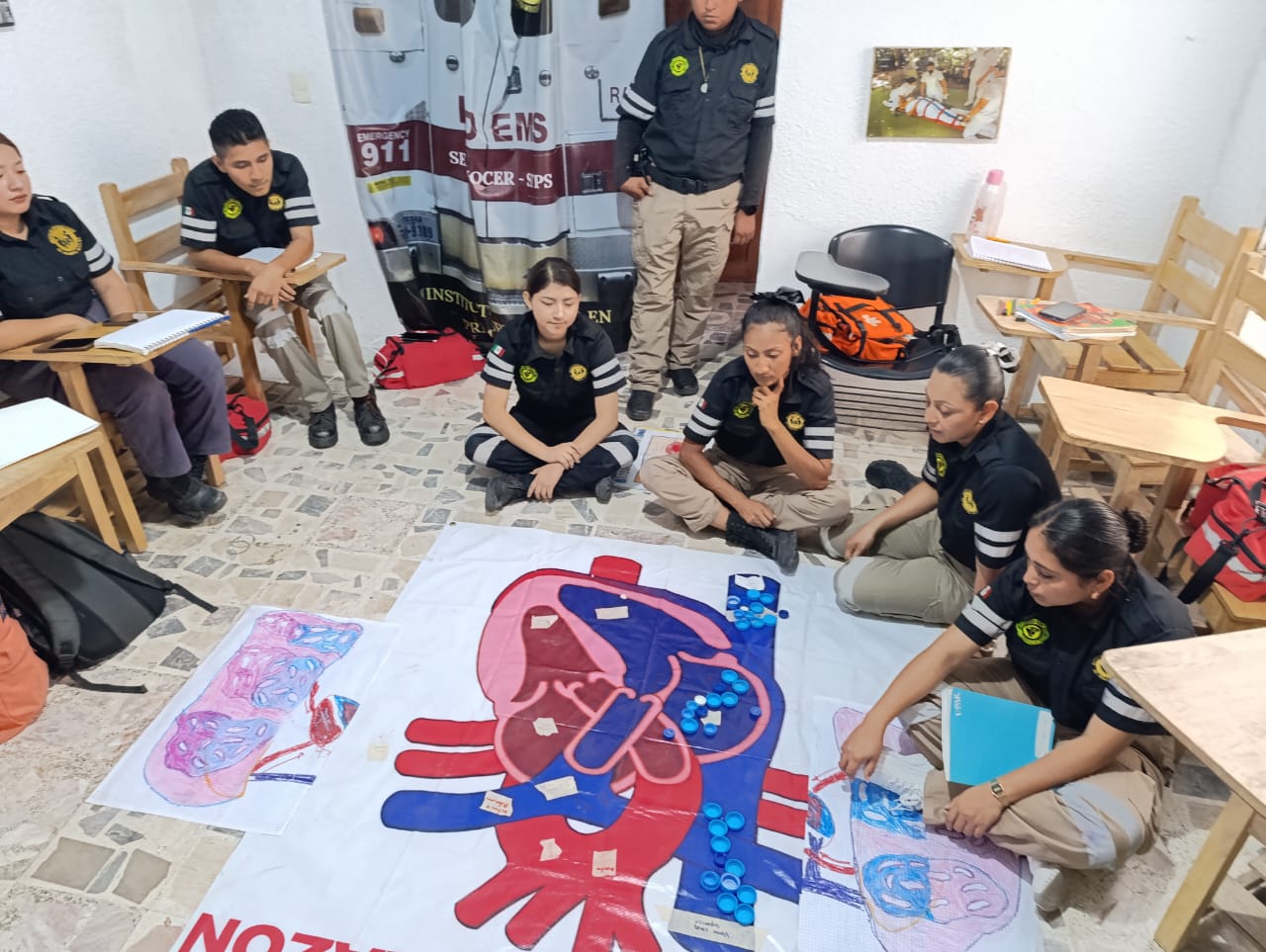 Group of people in uniforms discussing anatomical diagrams on the floor in a classroom setting.