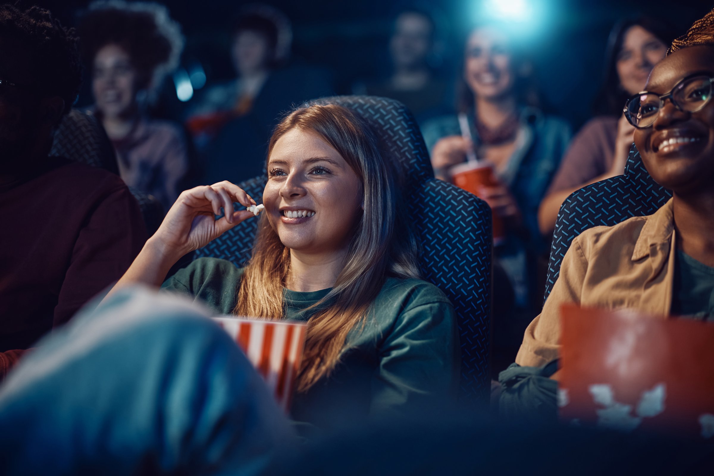 Happy woman eating popcorn during film screening at movie theatre.
