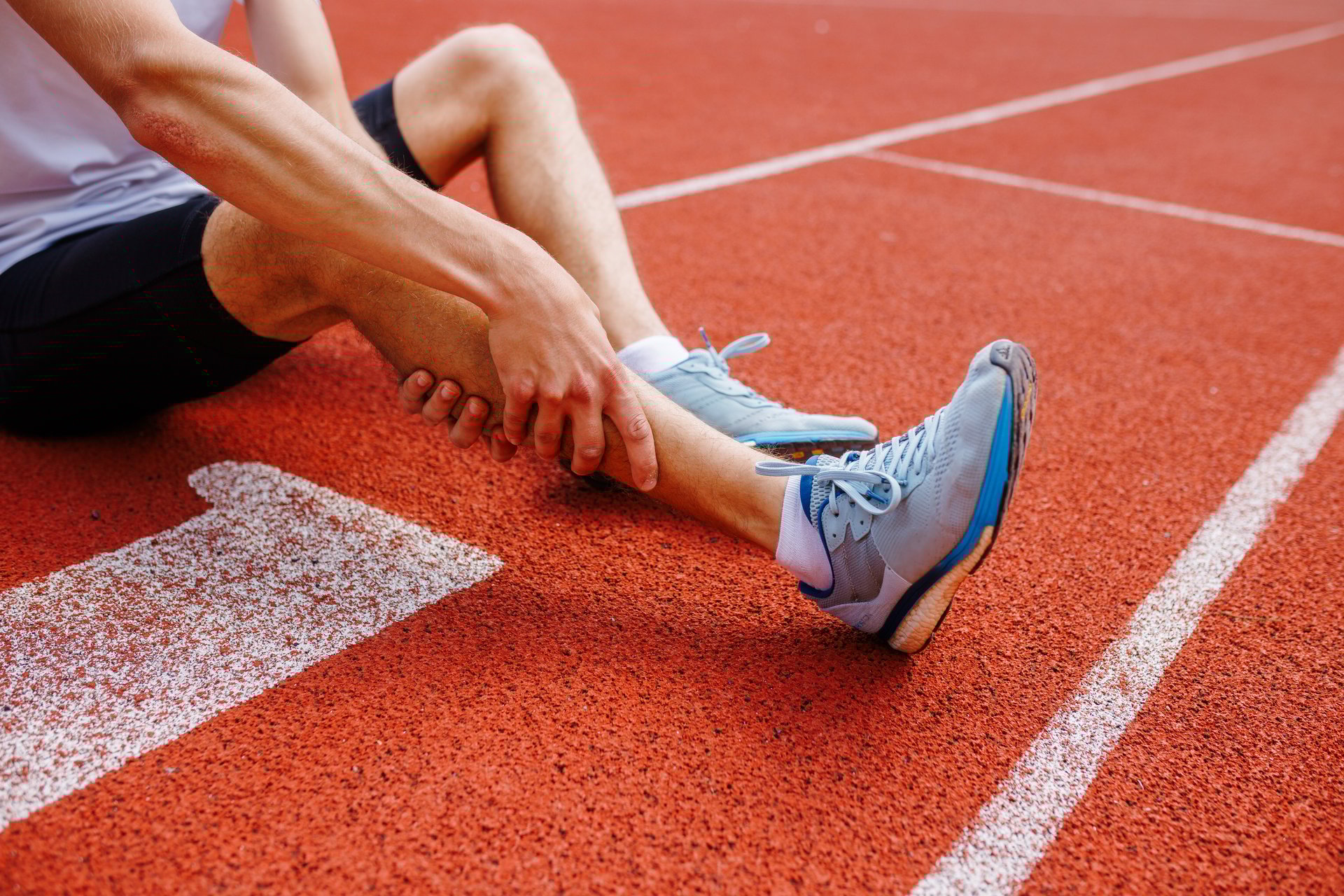 Athlete holding his leg injured after running at track and field stadium