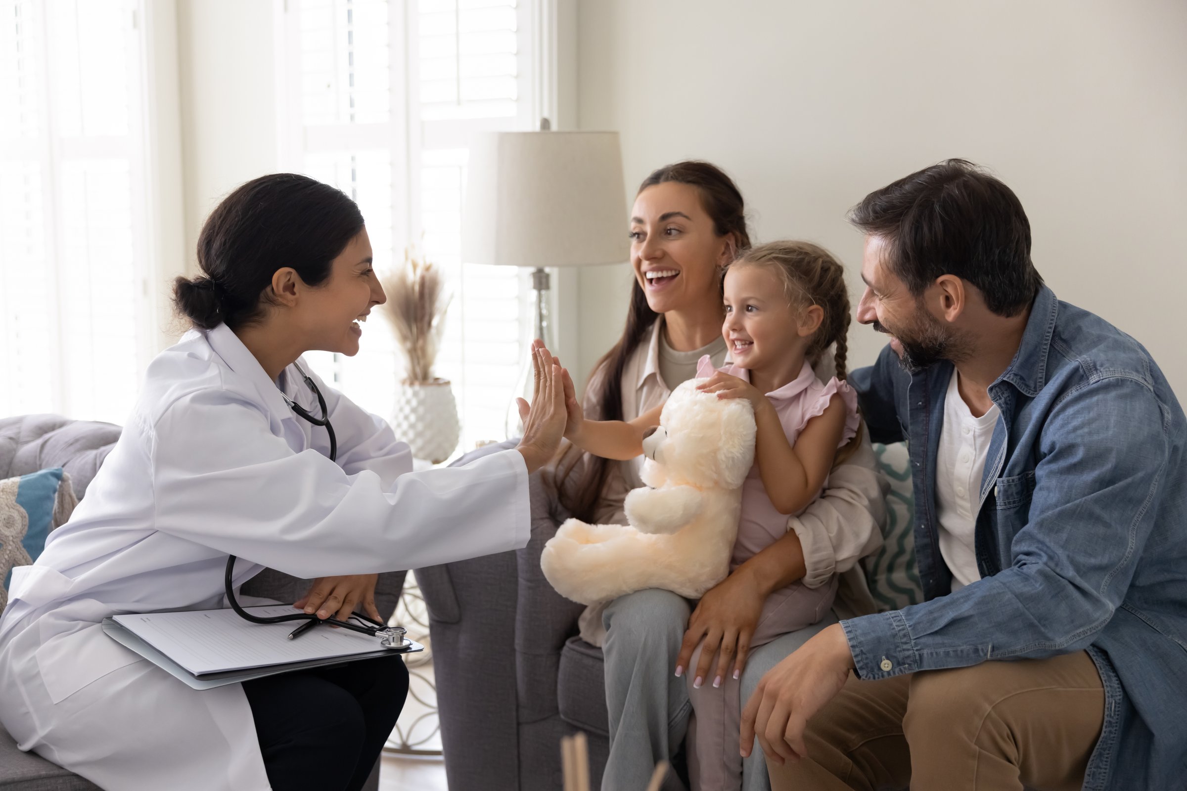 Happy doctor visiting little patient girl and her parents at home, giving high five hand gesture to positive healthy kid after successful therapy, examination, checkup, smiling, laughing