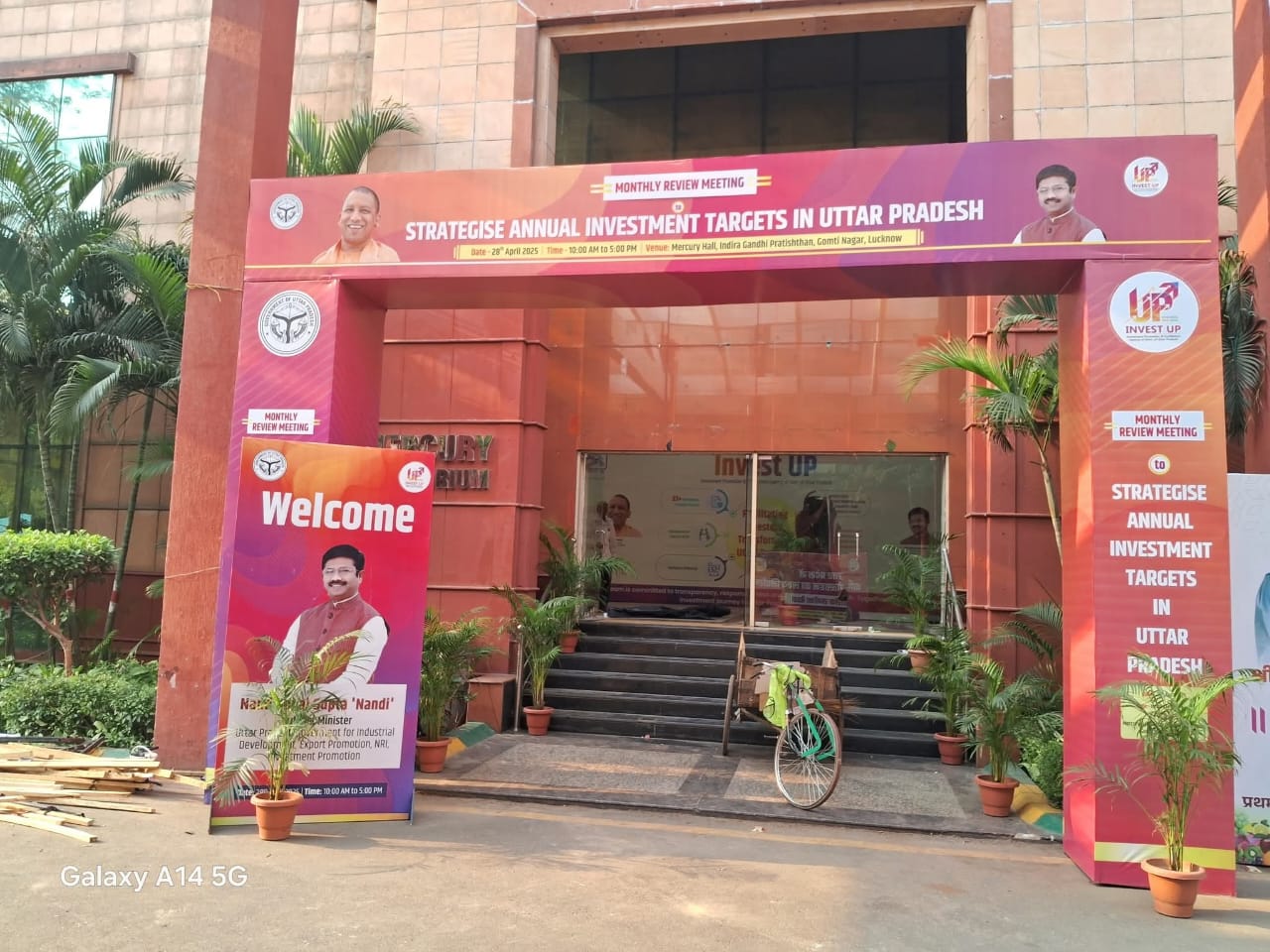 Entrance to an investment meeting venue in Uttar Pradesh with banners and a bicycle parked outside.