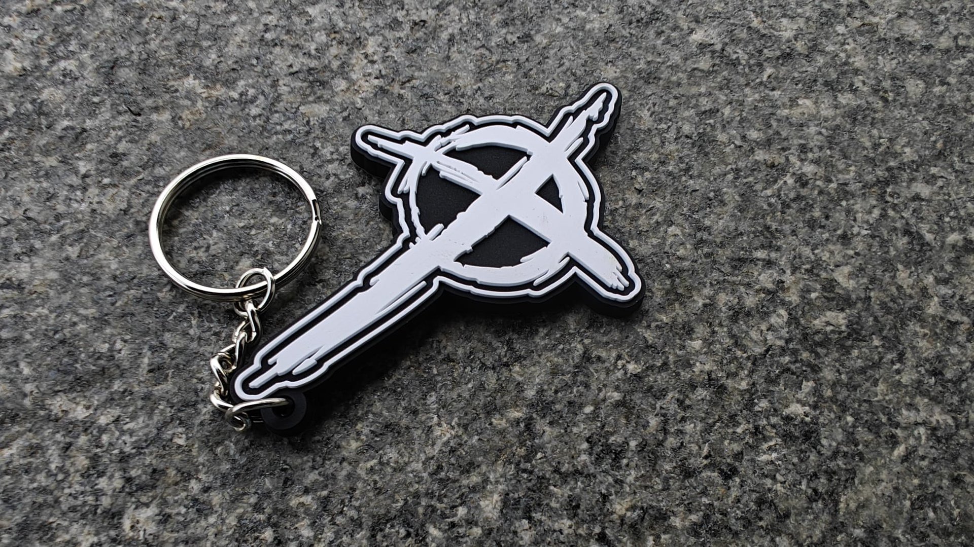 Keychain with a circular symbol featuring a stylized cross and circle design on a textured gray surface.