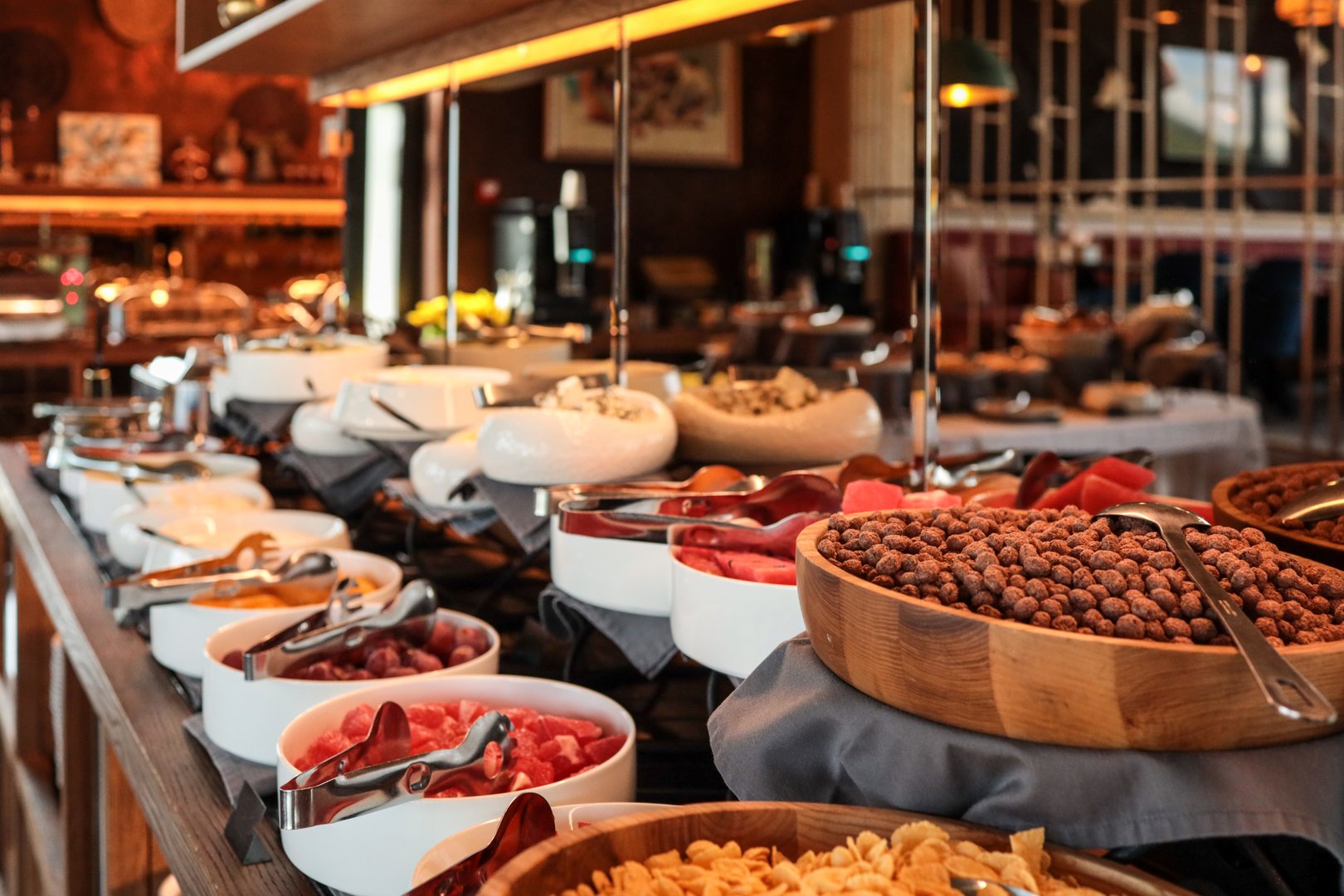 Rich hotel breakfast buffet with bowls of fresh fruits, cereals, nuts, cheeses, and cold cuts. Close-up view of a variety of colorful dishes on a stylish counter with serving utensils.