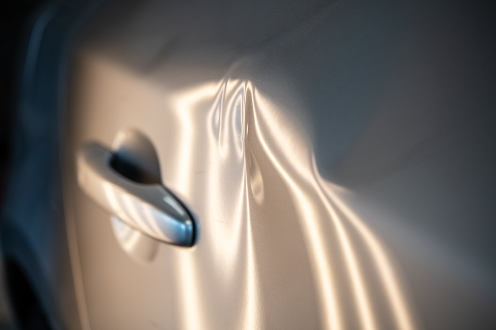 Close-up of a car door featuring multiple dents illuminated by soft lighting, illustrating the effects of minor accidents. Essential for insurance claims and automotive repair services, showcasing the need for professional restoration.