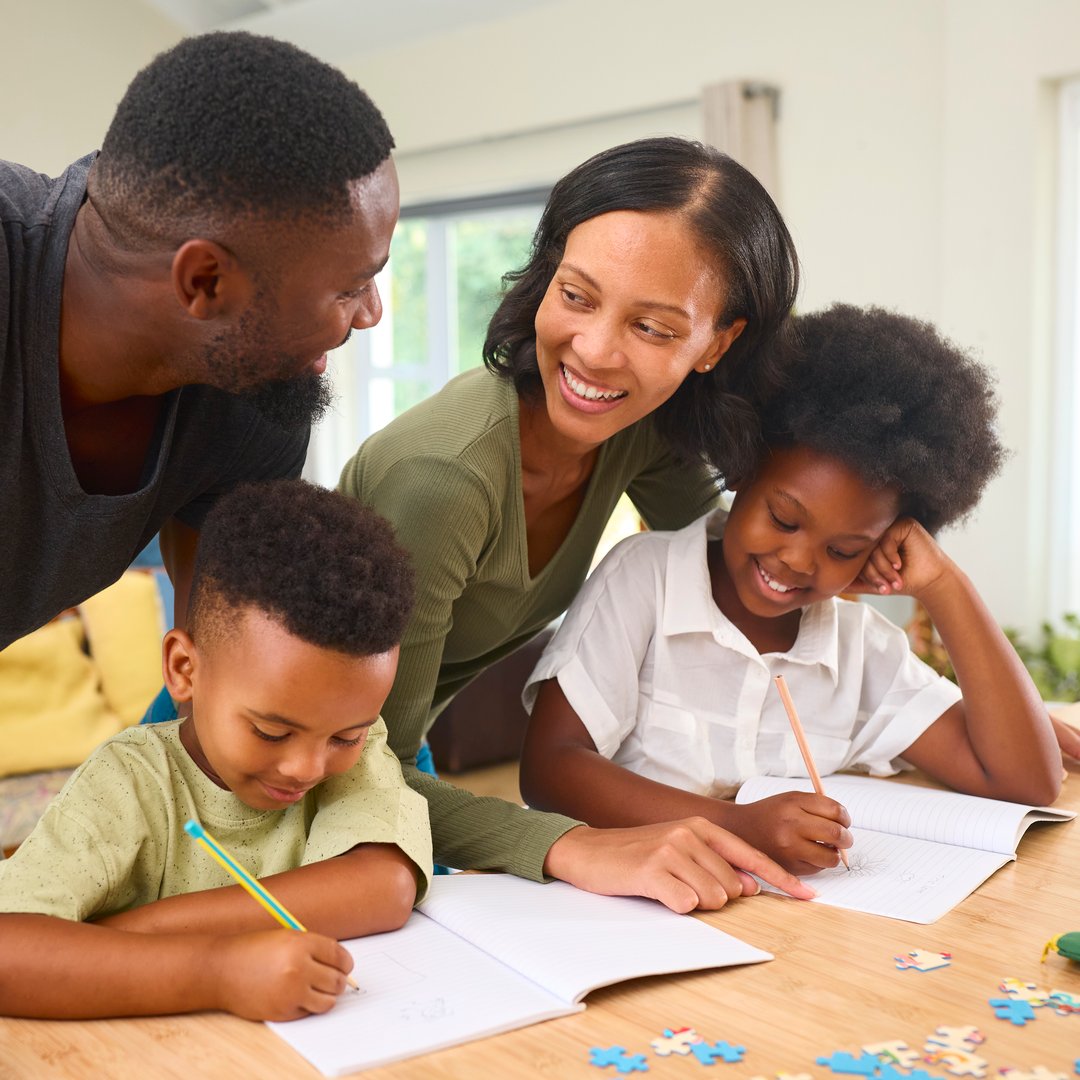 Family Indoors At Home With Parents Helping Children With Homework Sitting At Table