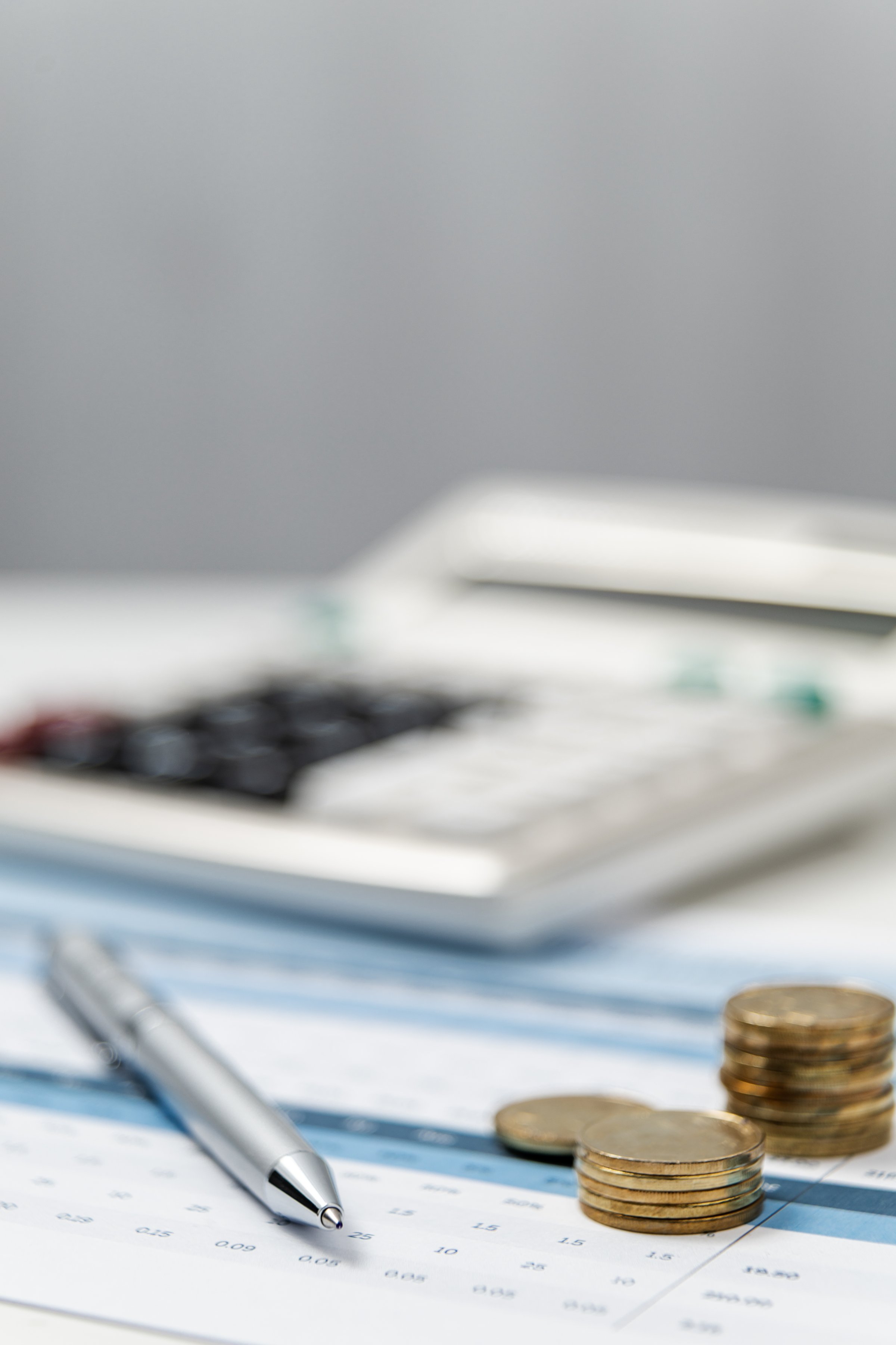 A calculator, stacked coins, and a pen lay on a financial tracking sheet, emphasizing budgeting and expense management in an office setting.