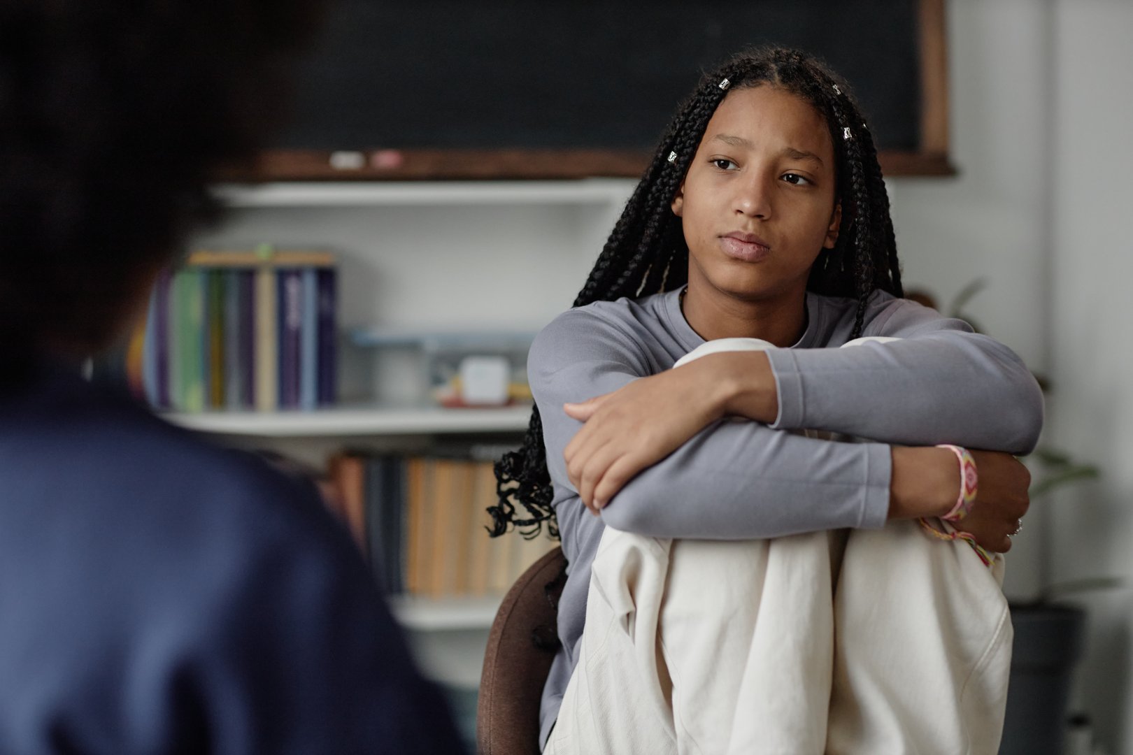 Portrait of young African American teenage girl listening to therapist or school counsellor during one on one meeting copy space