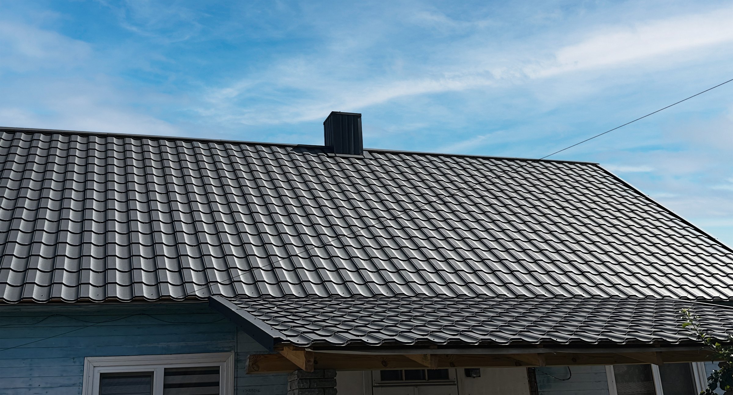 Close-up house roof with steel roofing sheet. Traditional metal shingle tiles. Black modular tile effect roof panel. Profiled metallic corrugated pantile as clay or concrete slate. Building's covering