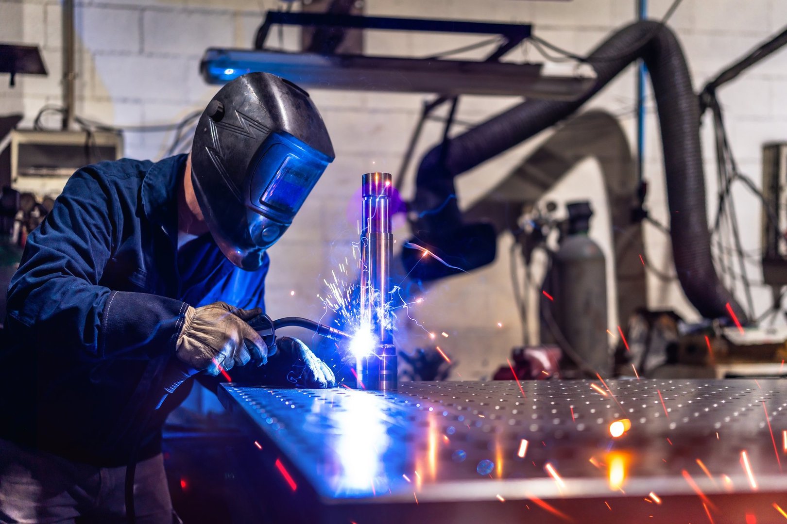 Unrecognizable man with safety goggles and gloves working in a factory welding pieces of metal