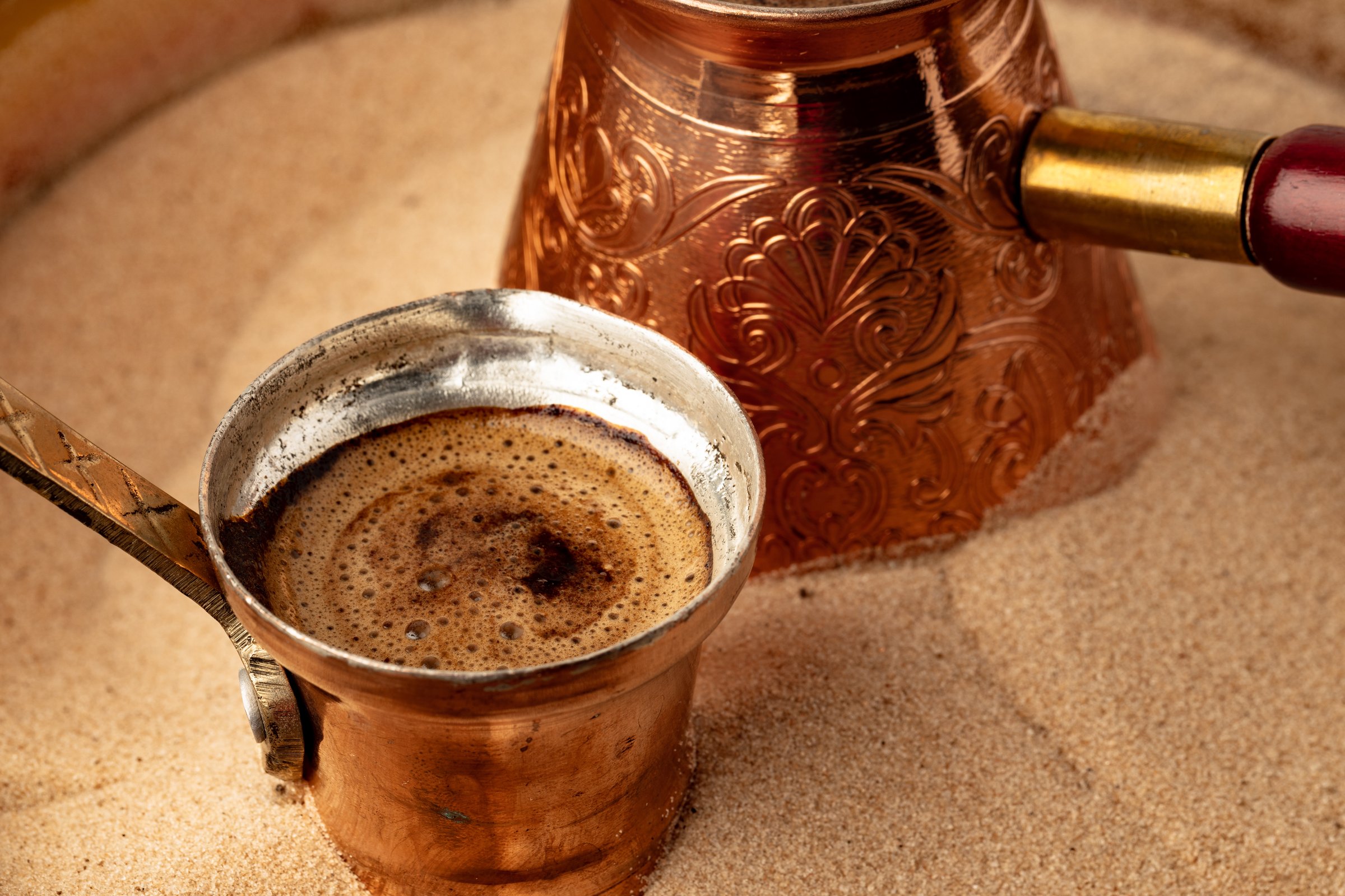 Copper turk with coffee brewing in sand close up.