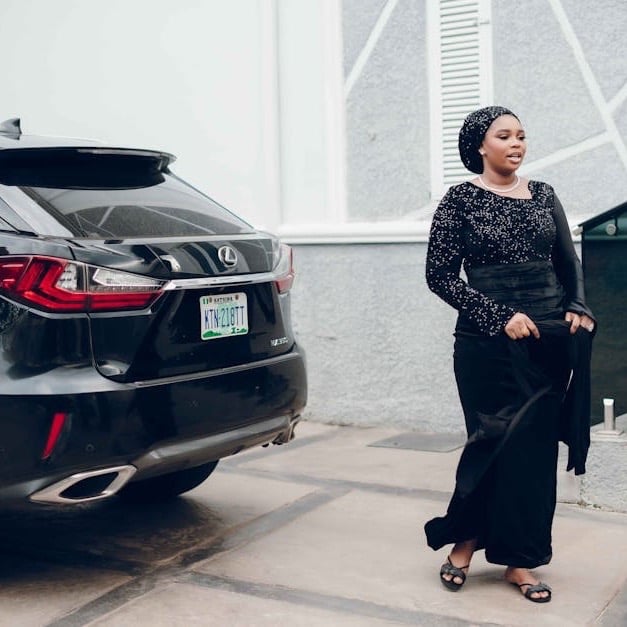 Woman in a black sequined dress standing next to a black Lexus SUV in a driveway.