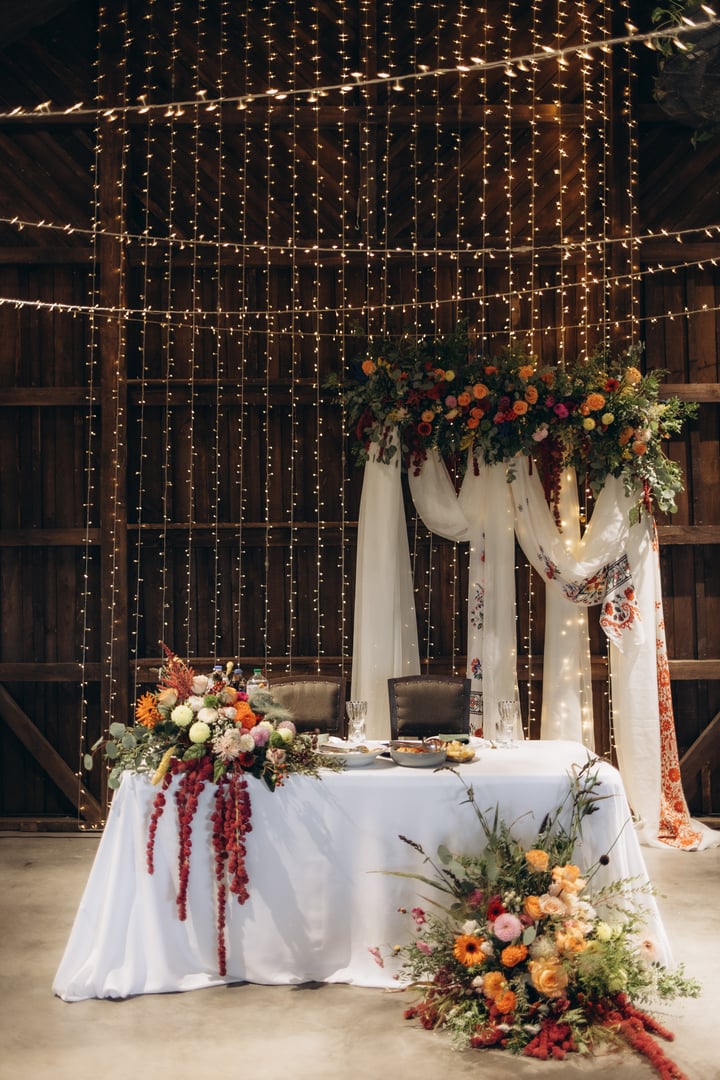 Elegant and romantic wedding reception setup featuring rich floral arrangements and string lights in a rustic barn. Ideal for celebrations, ceremonies, and venues with a charming countryside aesthetic.