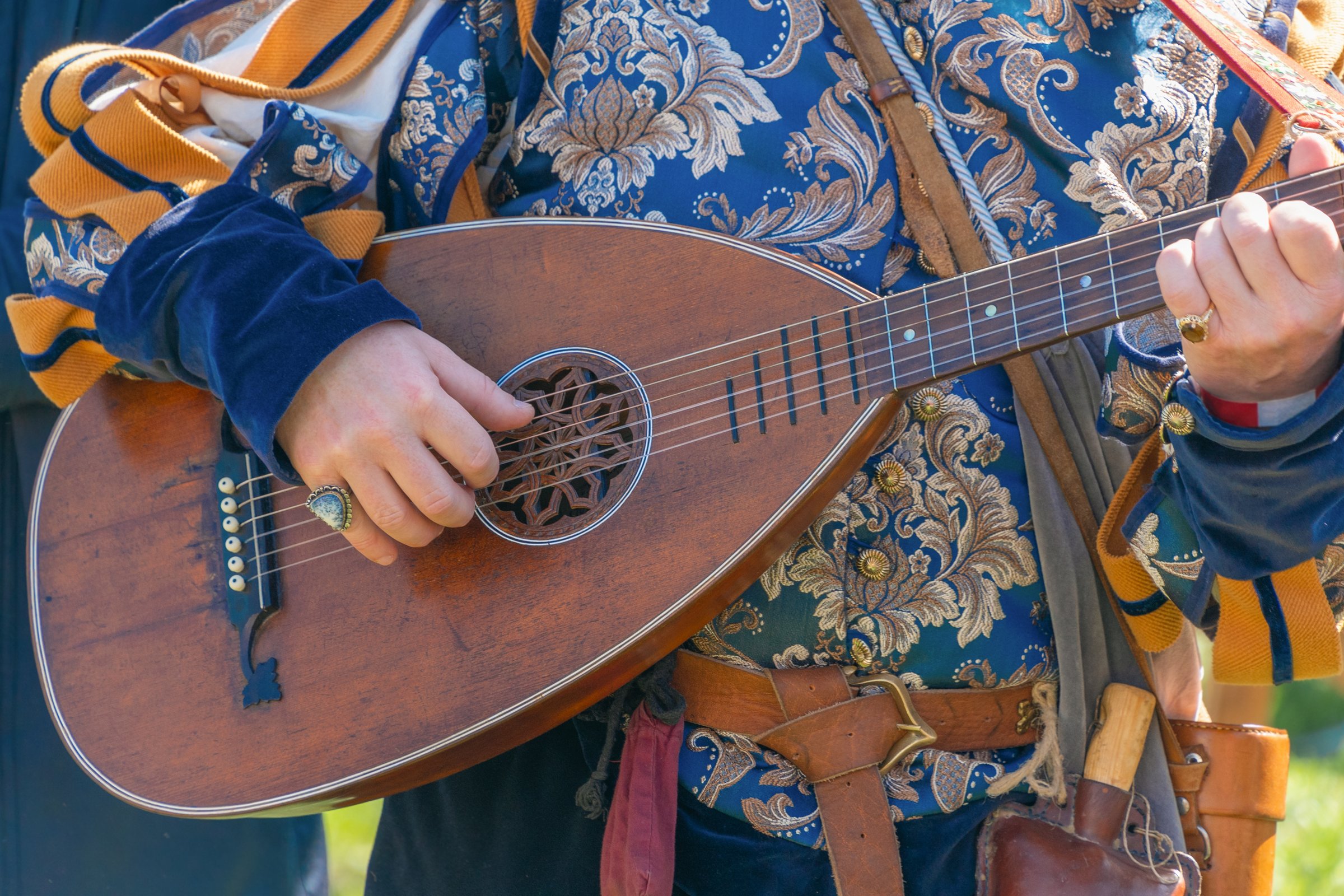 Mature caucasian male playing lute in historical costume at outdoor festival.