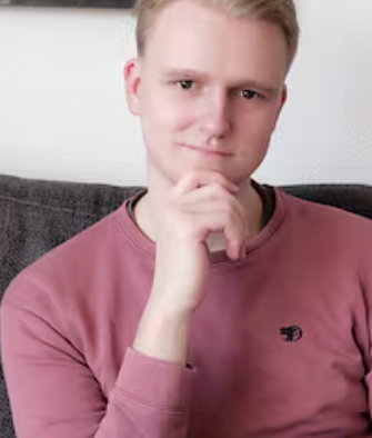 Person in a pink sweatshirt sitting on a gray couch, resting their chin on their hand, with a thoughtful expression.