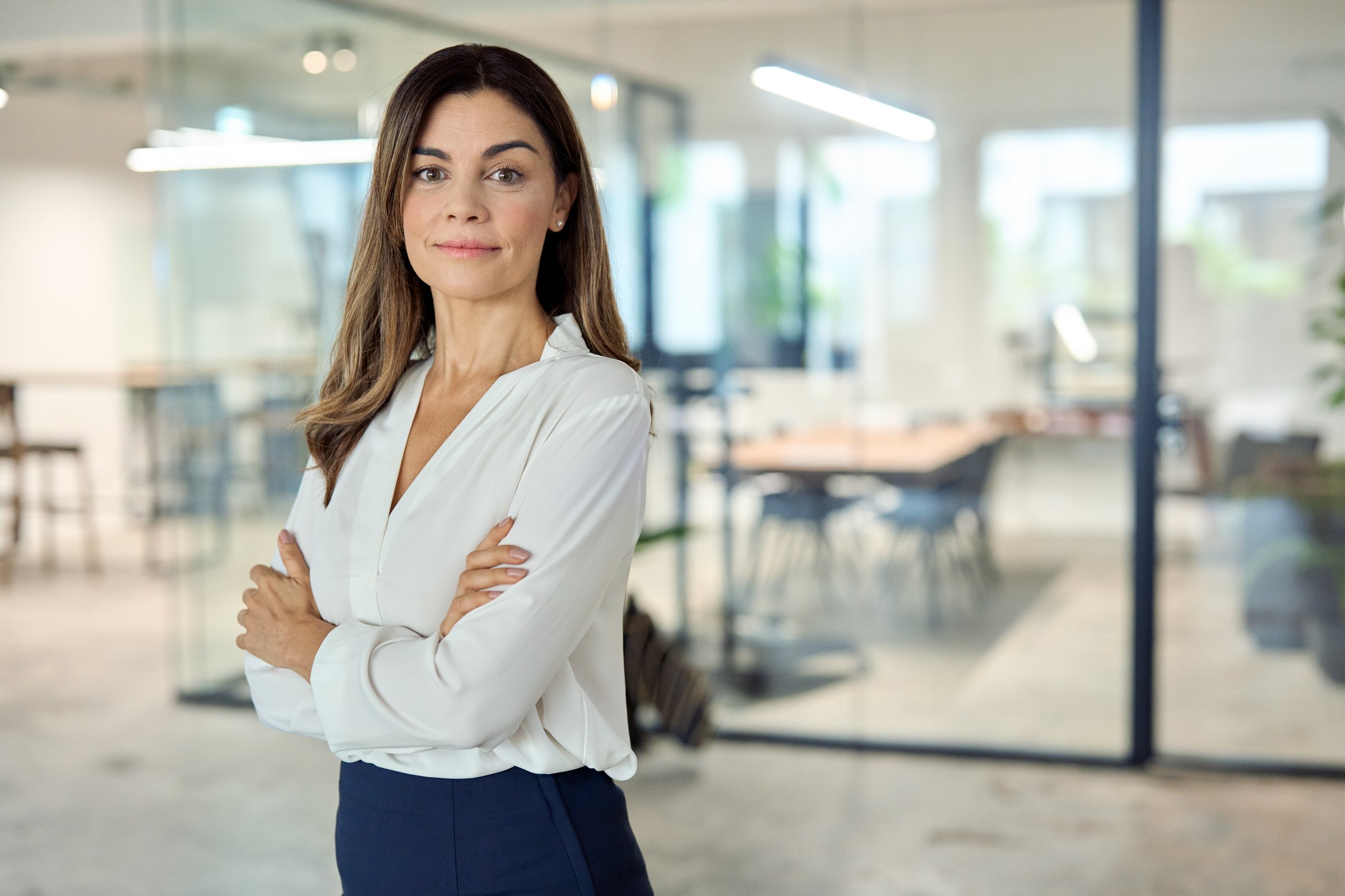Confident mid aged Latin professional business woman corporate leader, happy mature female executive, elegant lady manager of middle age standing in office arms crossed looking at camera, portrait.
