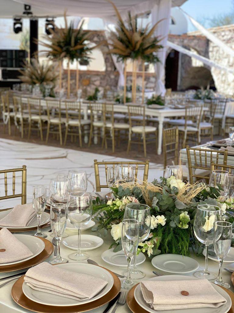 Elegant table setting at an outdoor event with gold chairs, floral centerpieces, and neatly arranged glassware and plates.