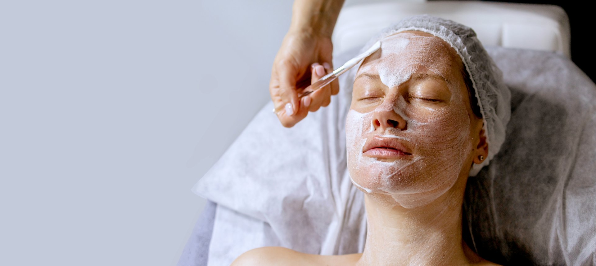 Banner of Middle aged female receiving facial anti aged massage in beauty salon. Skincare concept. Cosmetology specialist making lifting massage, appling cosmetic product to facial skin with brush