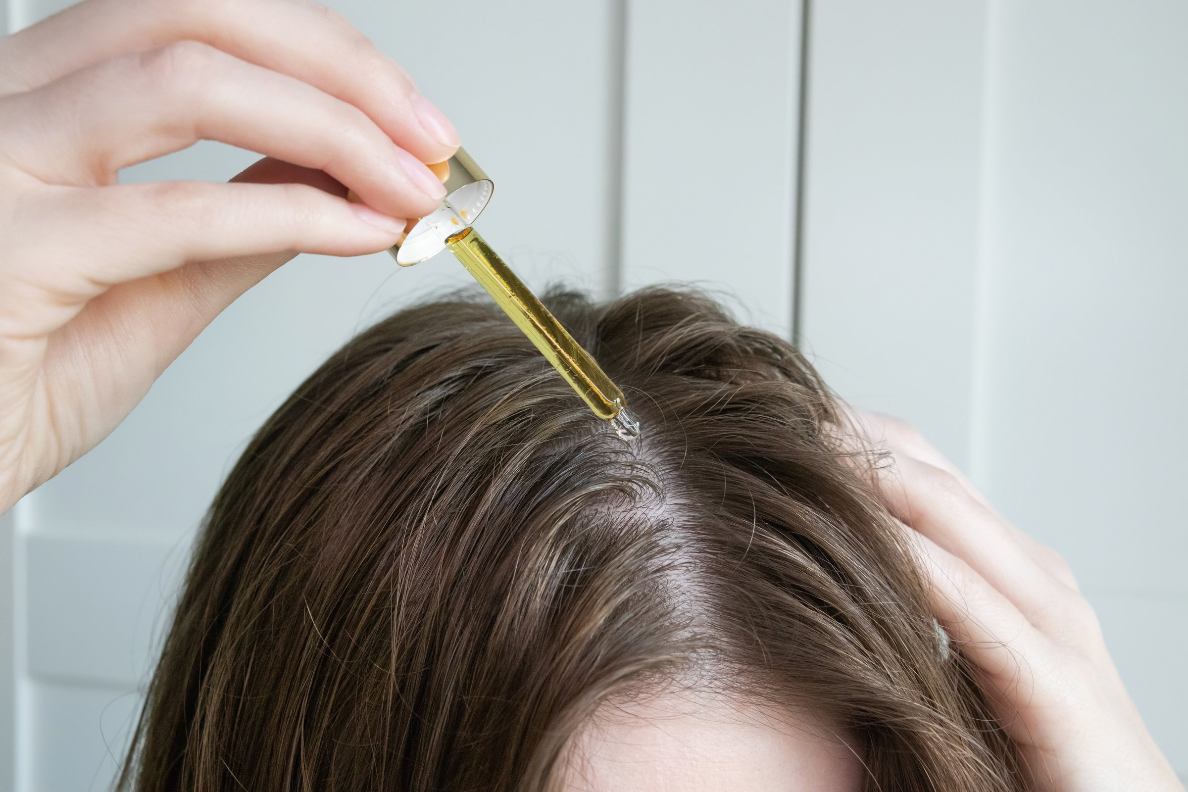 Close up of young woman dropping hair oil, serum on scalp to prevent dryness, dandruff, hair loss.