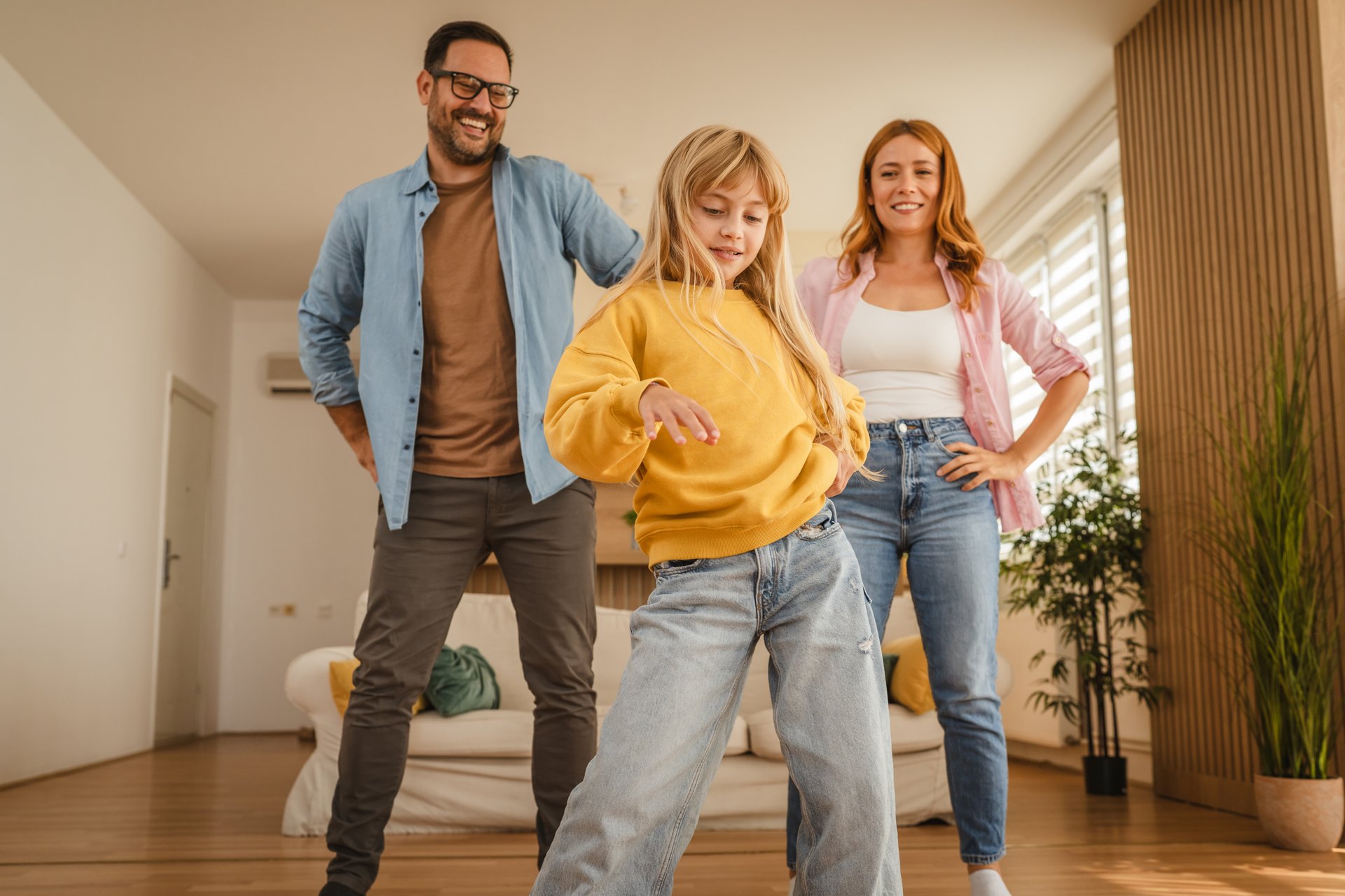 Happy family, a father, mother, and child, dancing with energy and having fun at home, sharing joyful moments and strengthening their bond in a bright living space