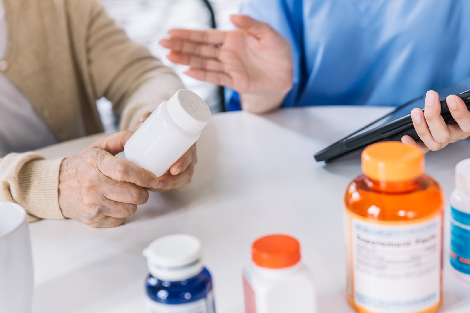 Close up hands of a senior woman holding a medical bottle and asking information from the nurse before administering medication. Caregiver visit at home. Home health care and nursing home concept.