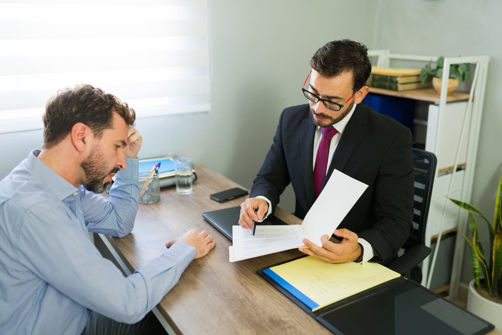 Male client receiving legal advice from a lawyer in a professional office setting, focusing on serious discussion