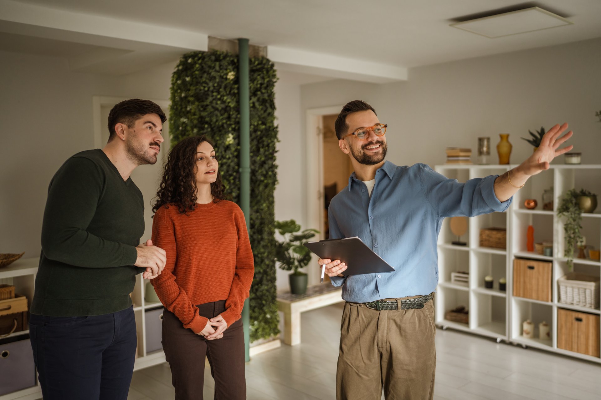 Real estate agent guiding a smiling young couple through a modern apartment during a property viewing as they discuss options for their future home