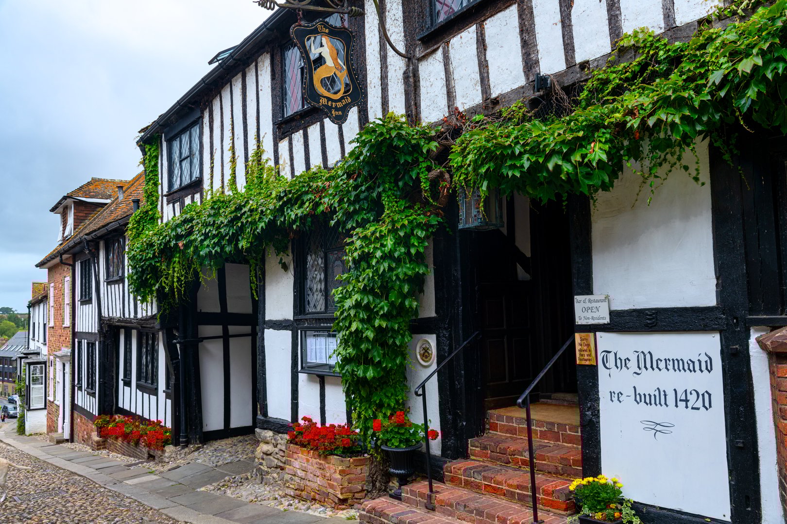 Color image depicting the charming cobbled Mermaid Street in the historic, medieval town of Rye in the southeast of England. The street is lined with Tudor-style cottages receding into the distance.