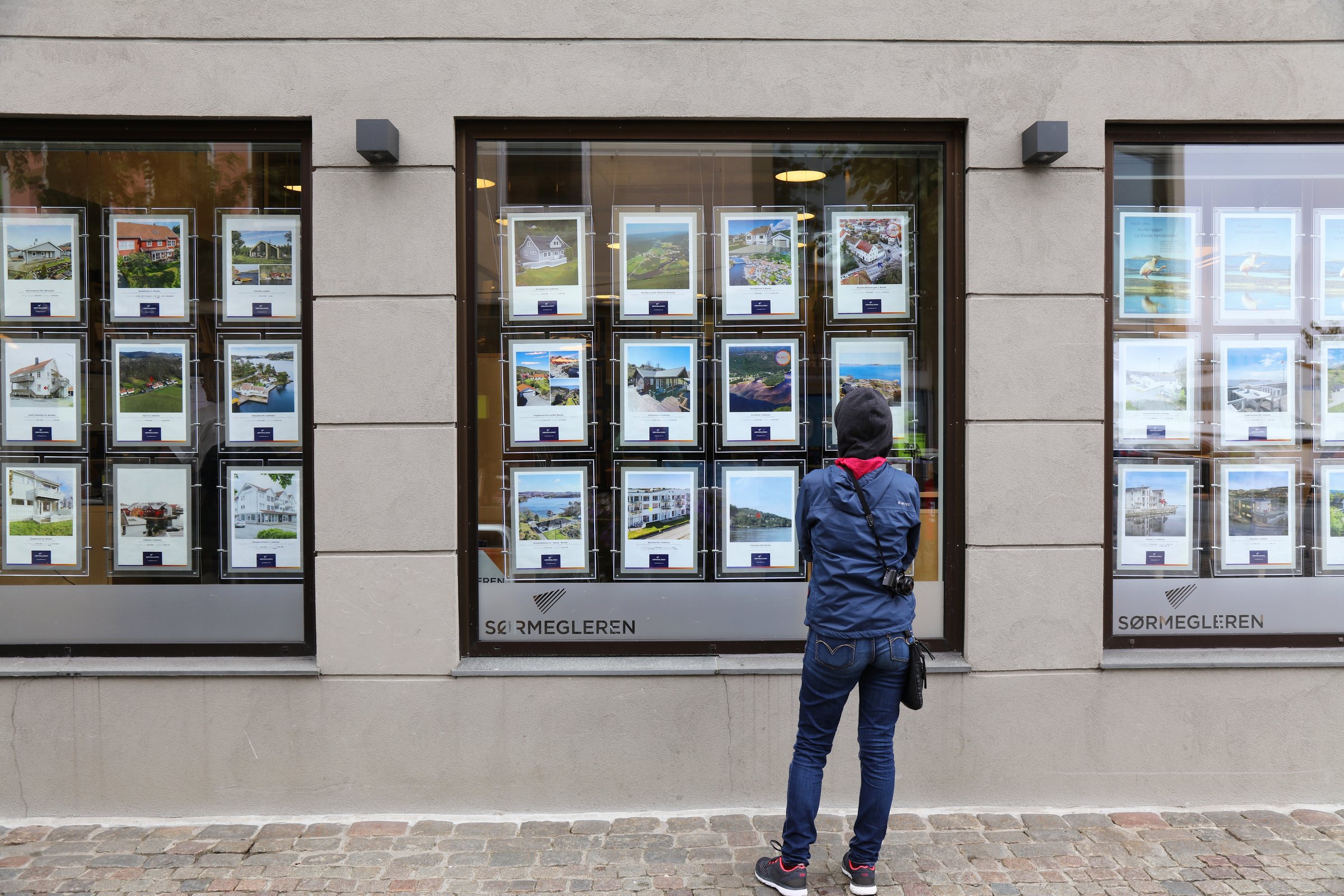 Person analyzes real estate offers of a real estate agency window in town of Mandal in Vest-Agder county of Norway.