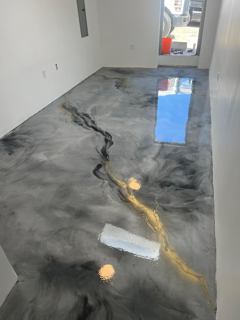 Gray epoxy floor with a marbled design featuring black and gold veins, reflecting light in a bright, minimal room.