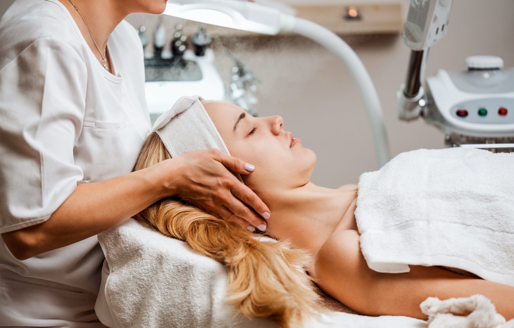 Nail technician giving manicure treatment in well-lit modern salon with green seating area. Client receiving professional nail care while engaged in friendly conversation