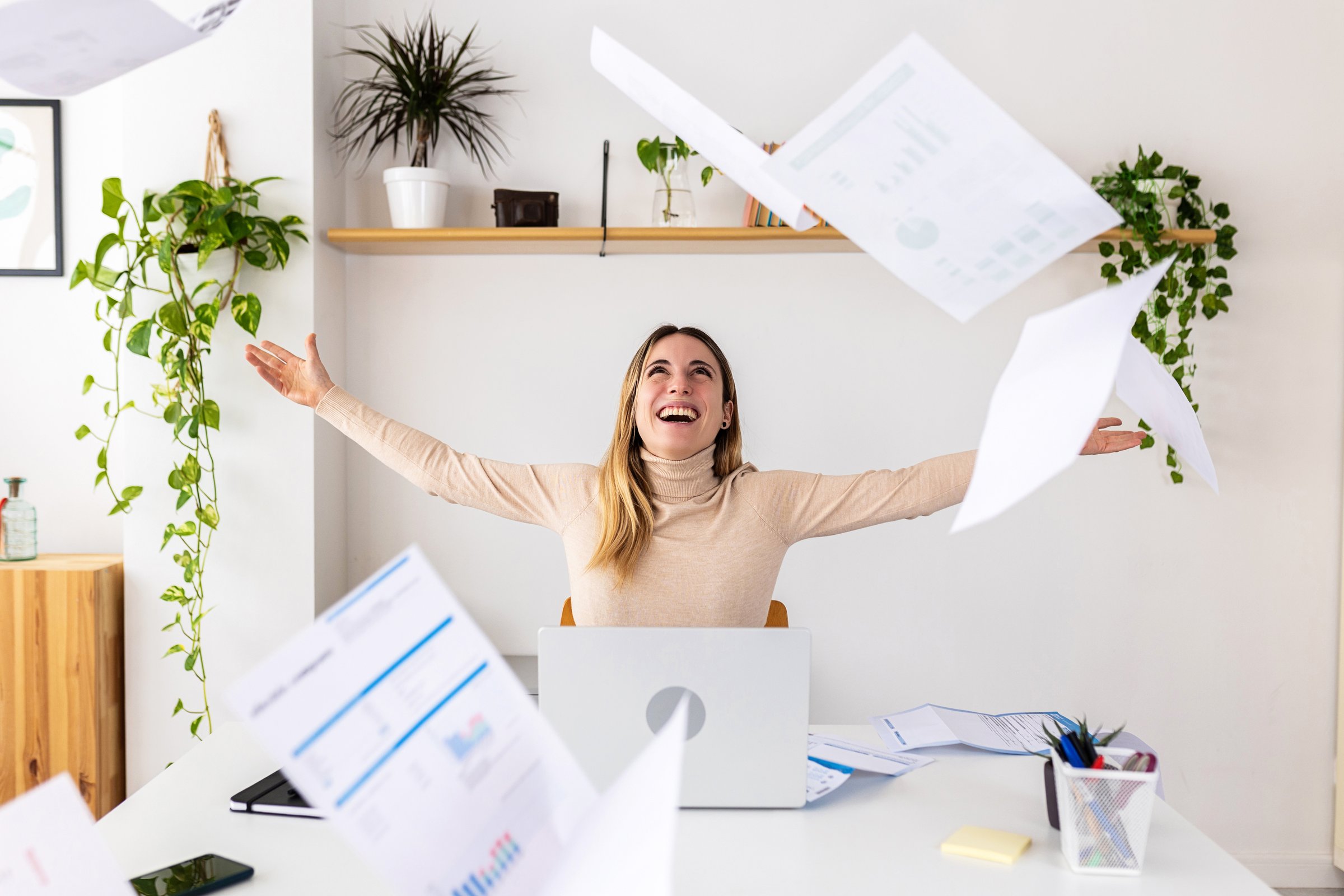 Young excited fun entrepreneur woman throwing papers celebrating business success at office