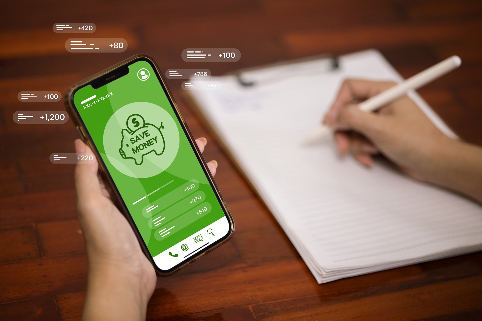 Hand holding smartphone with money saving app, financial data, and transaction notifications, representing online banking, personal finance, and savings management.