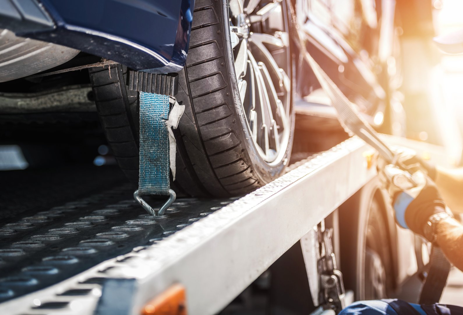 Closeup of Vehicle Wheel Secured on the Tow Truck with Tie Down Straps for Safe Transportation. Breakdown Assistance. Automotive Industry.
