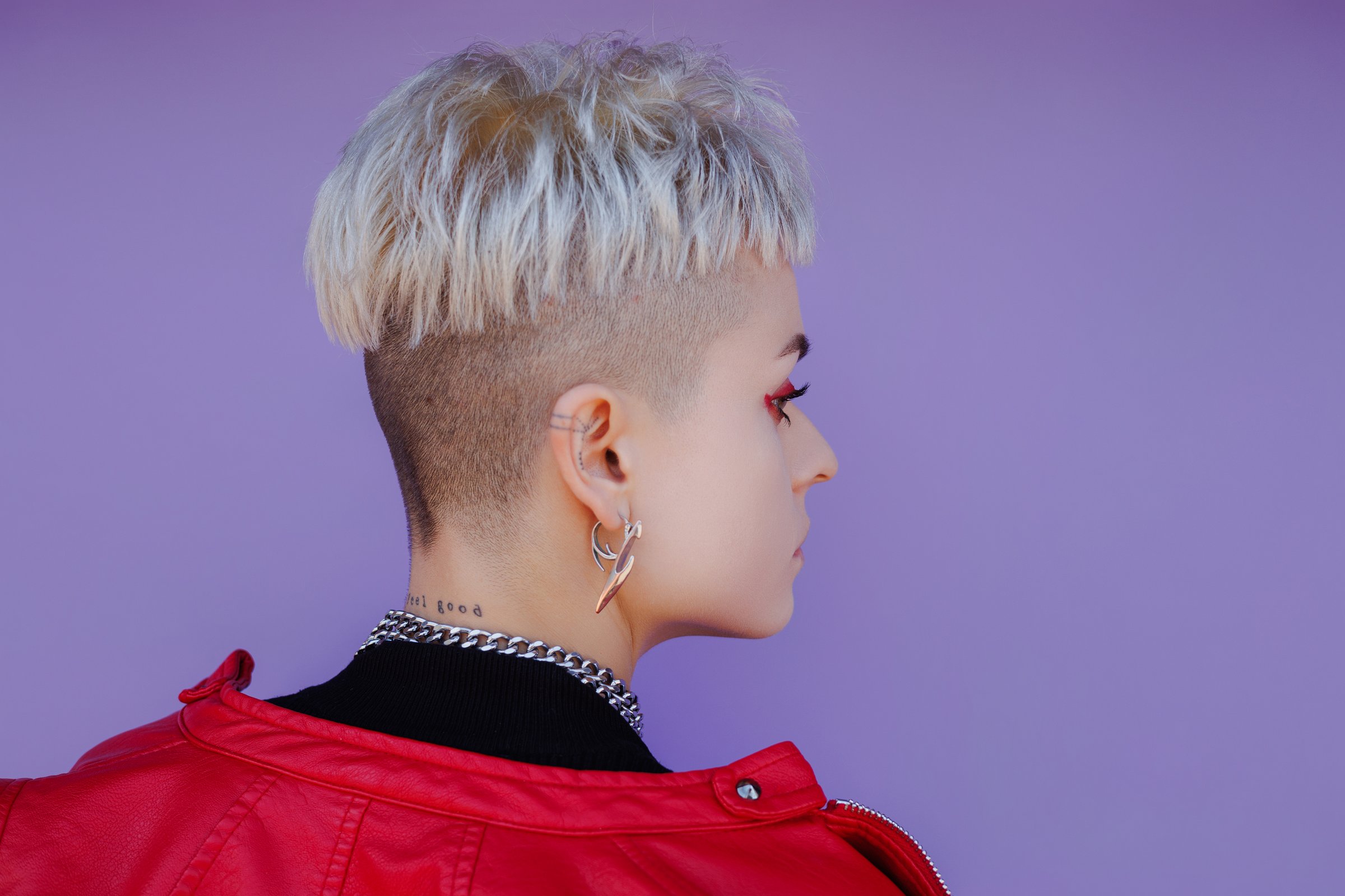 Stylish woman with tattoo on neck posing on purple backdrop