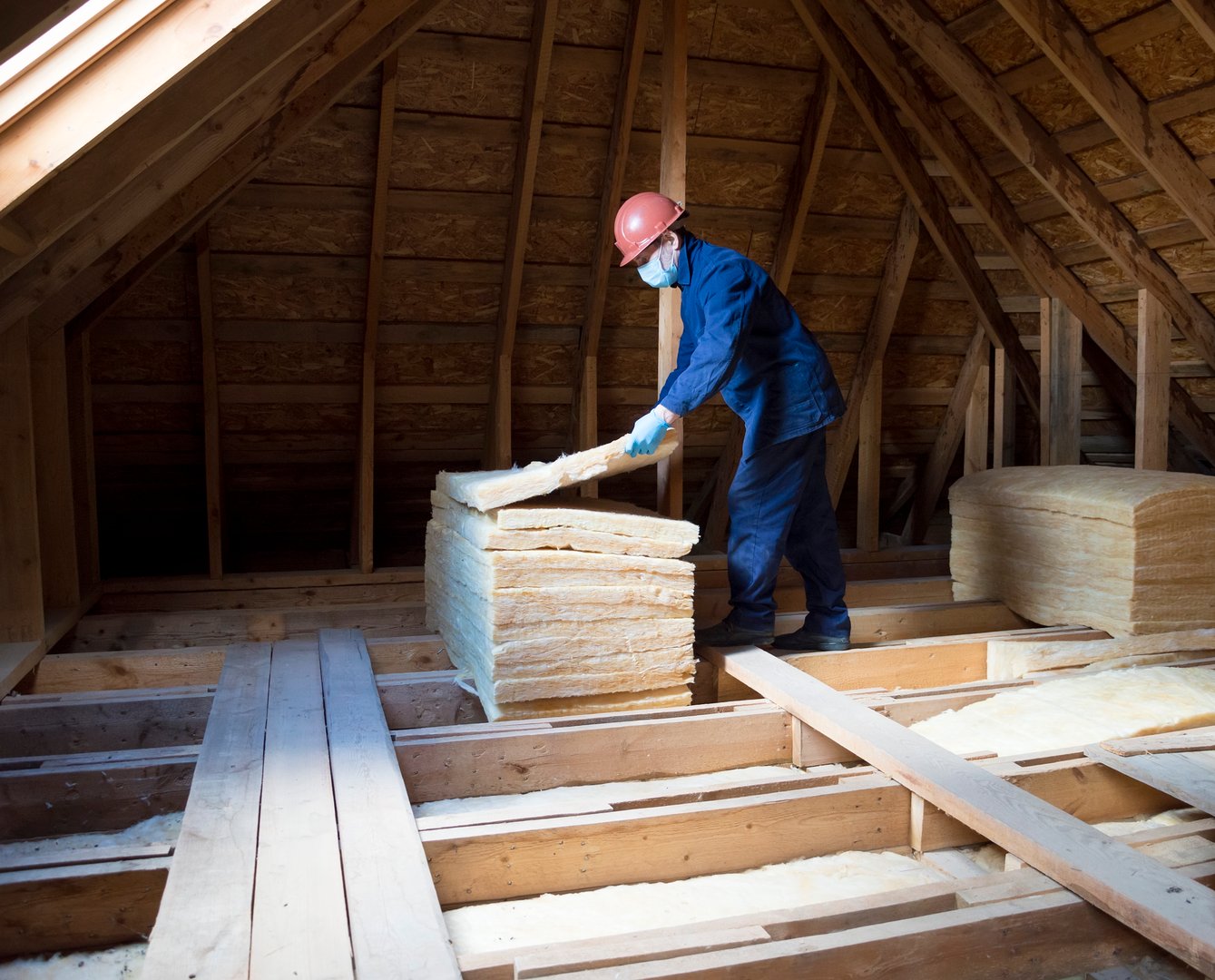 Roof insulation. A worker puts glass wool insulation in the attic.