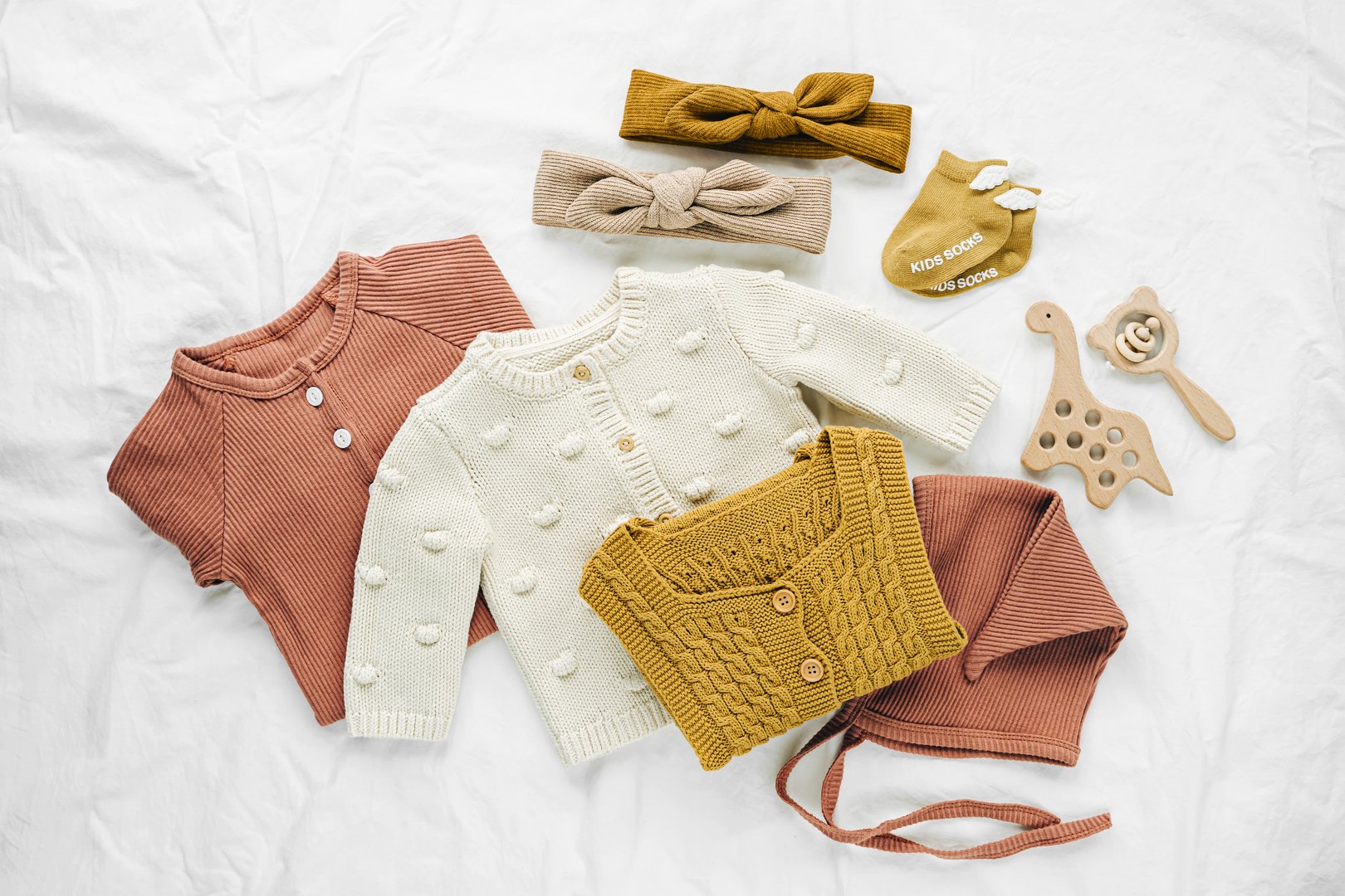 Set of  baby rompers, hat,  hairband and  knitted jumper on white bed. Fashion  baby clothes and accessories. Flat lay, top view