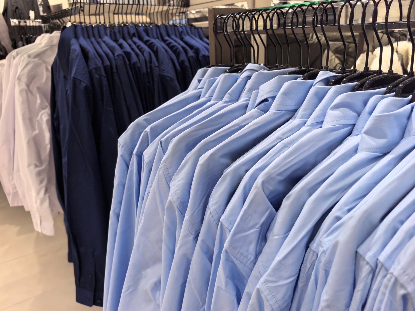 Rows of neatly hung dress shirts in shades of blue and white fill this modern store. The clean, crisp fabric highlights a stylish selection for formal and casual wear.