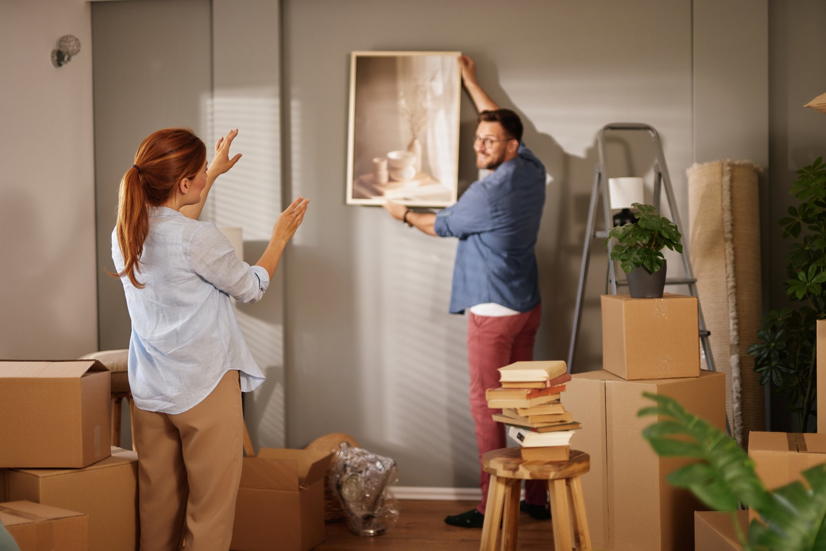 Young couple is decorating and hanging pictures on the wall in their new apartment
