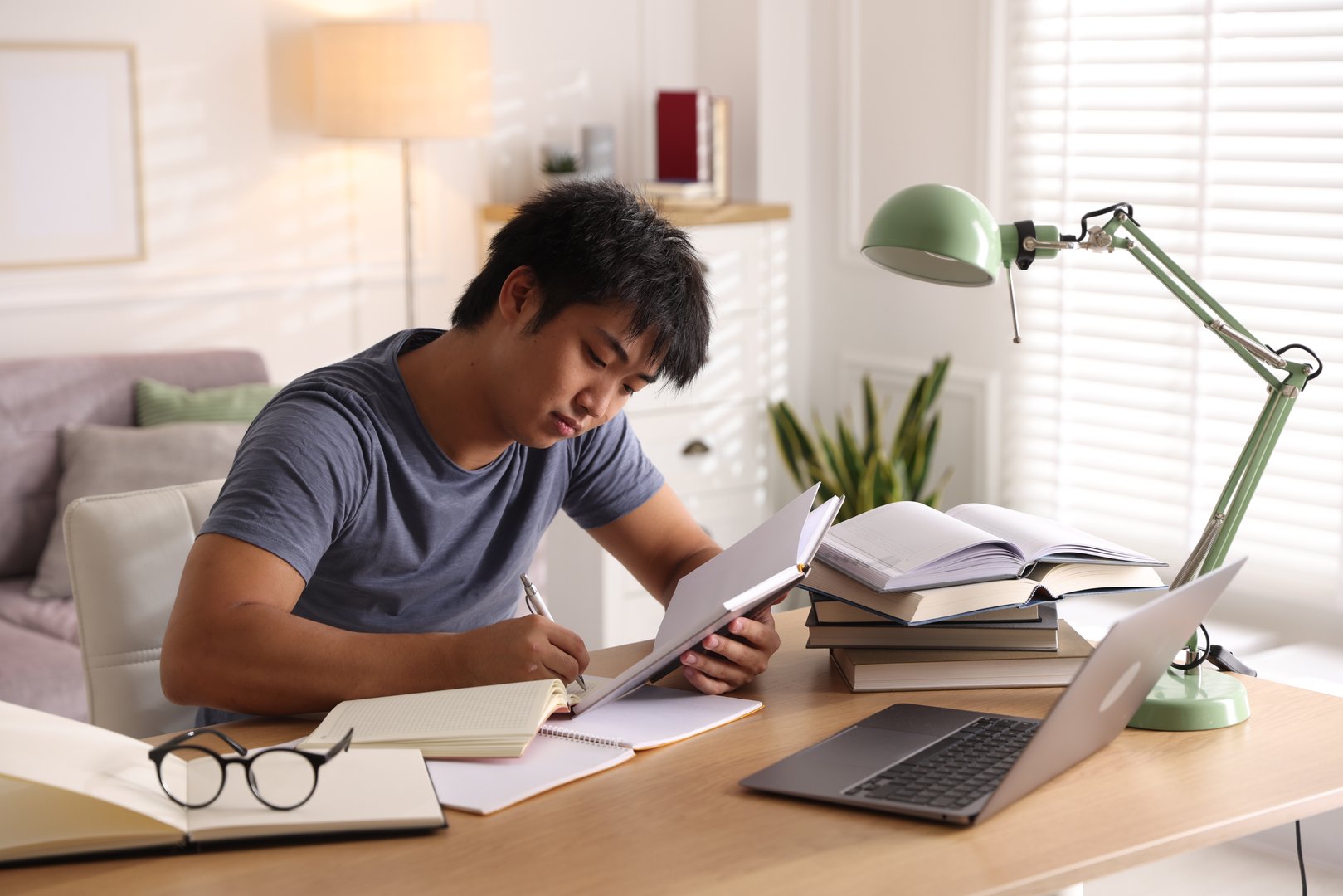 Student with laptop and books preparing for exam at table indoors