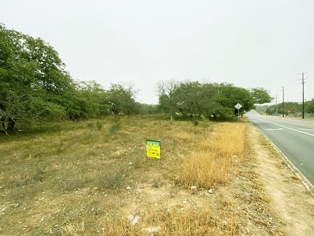 Vacant grassy lot with trees beside a road, featuring a For Sale sign in the foreground.